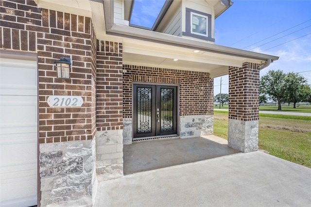 view of exterior entry with brick siding, french doors, and covered porch