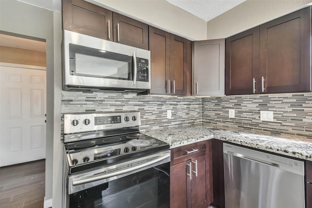kitchen featuring backsplash, wood finished floors, light stone countertops, and stainless steel appliances