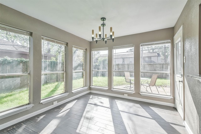 unfurnished sunroom with baseboards, a notable chandelier, and wood-type flooring