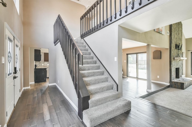 staircase with baseboards, wood finished floors, and a high ceiling