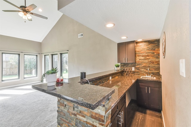 kitchen featuring dark stone counters, high vaulted ceiling, a sink, ceiling fan, and a peninsula