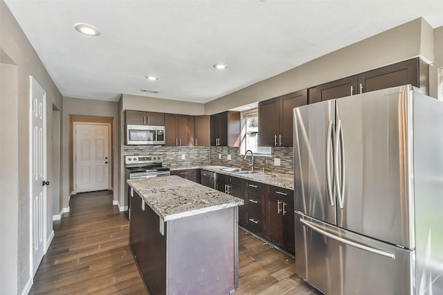 kitchen featuring a center island, dark brown cabinets, a sink, decorative backsplash, and appliances with stainless steel finishes