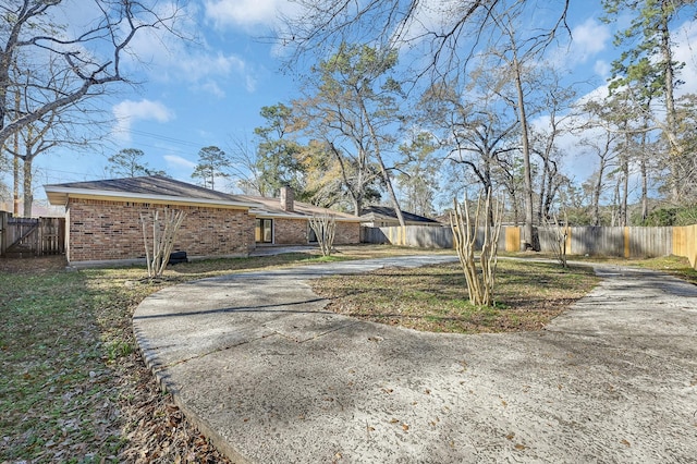 exterior space with brick siding, driveway, a chimney, and a fenced backyard