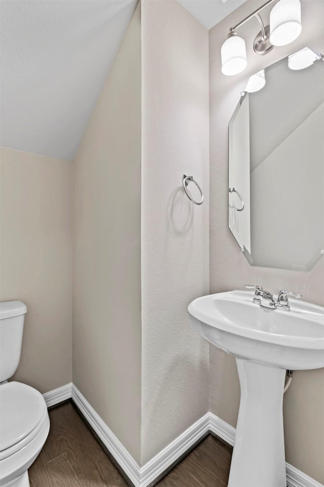 half bath with toilet, baseboards, vaulted ceiling, and wood finished floors