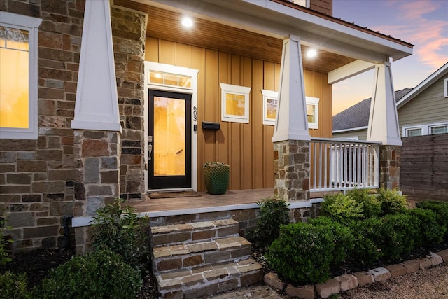 exterior entry at dusk with a porch, stone siding, and board and batten siding