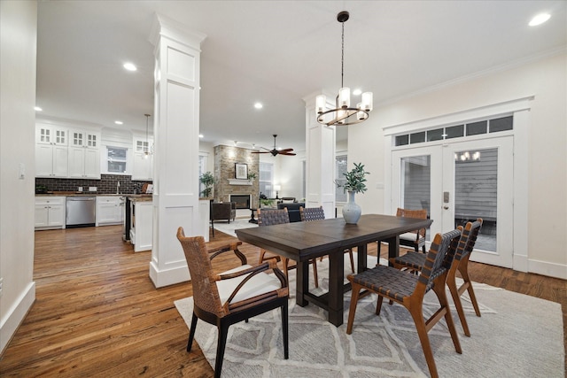 dining space featuring a stone fireplace, ceiling fan with notable chandelier, light wood-style flooring, ornamental molding, and recessed lighting