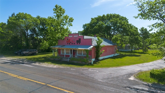 bungalow-style house featuring metal roof, a front lawn, dirt driveway, and covered porch