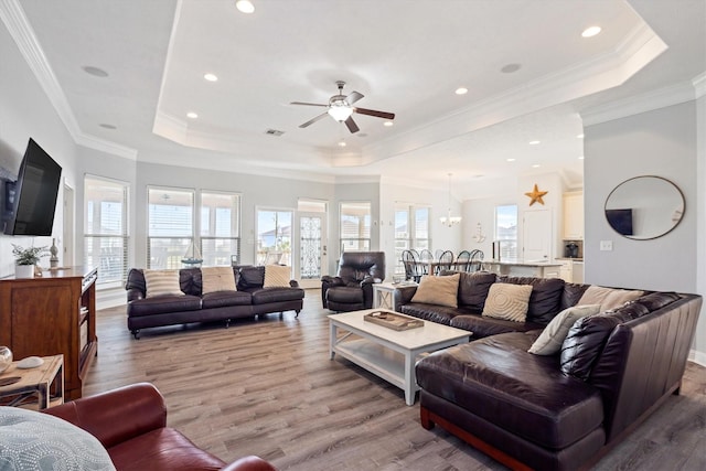 living area with a wealth of natural light, a ceiling fan, wood finished floors, and a raised ceiling
