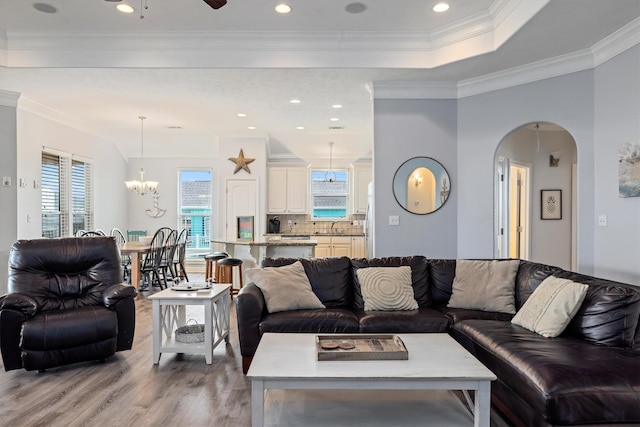 living area with arched walkways, light wood-type flooring, a healthy amount of sunlight, and a notable chandelier