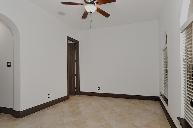 unfurnished room featuring baseboards, ceiling fan, and arched walkways