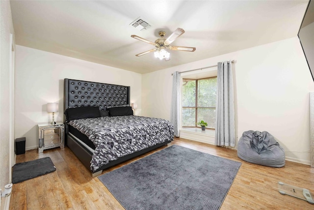 bedroom with a ceiling fan, visible vents, wood finished floors, and baseboards