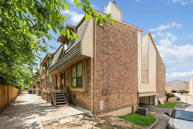 view of side of home featuring fence, a chimney, cooling unit, and brick siding