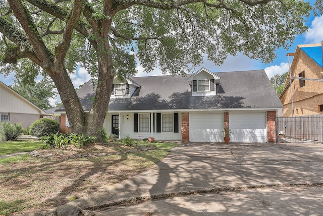 cape cod-style house featuring concrete driveway, fence, a garage, brick siding, and roof with shingles
