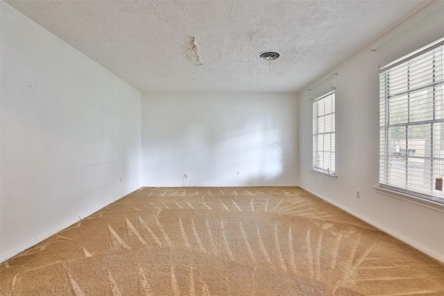 carpeted empty room with a textured ceiling, baseboards, and visible vents