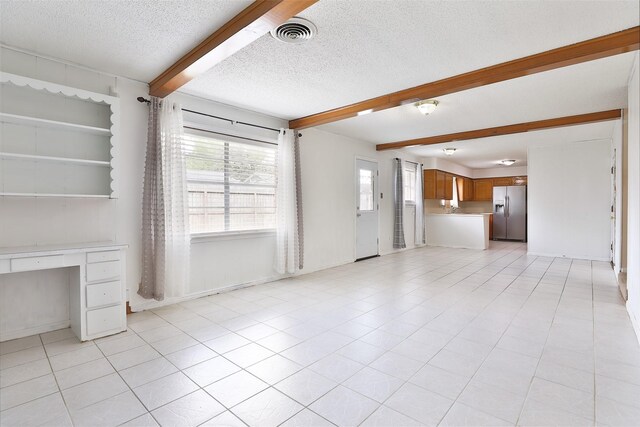 unfurnished living room with a textured ceiling, built in desk, light tile patterned flooring, beamed ceiling, and visible vents