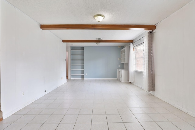 empty room featuring a textured ceiling, beam ceiling, built in shelves, and baseboards