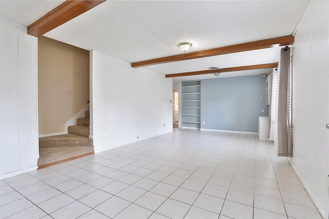empty room featuring stairway, a textured ceiling, light tile patterned flooring, built in features, and beamed ceiling