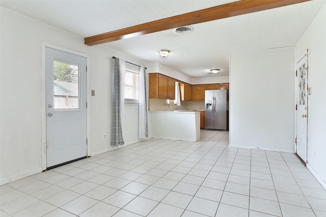 kitchen with brown cabinets, light countertops, visible vents, a peninsula, and stainless steel fridge