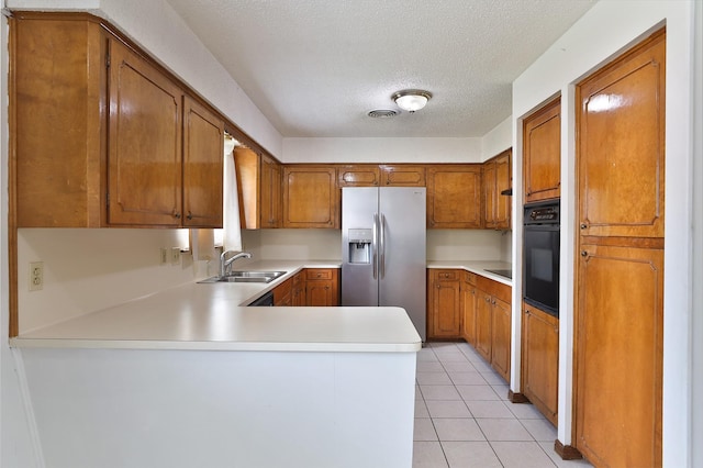 kitchen with stainless steel fridge with ice dispenser, a sink, black oven, a peninsula, and brown cabinetry