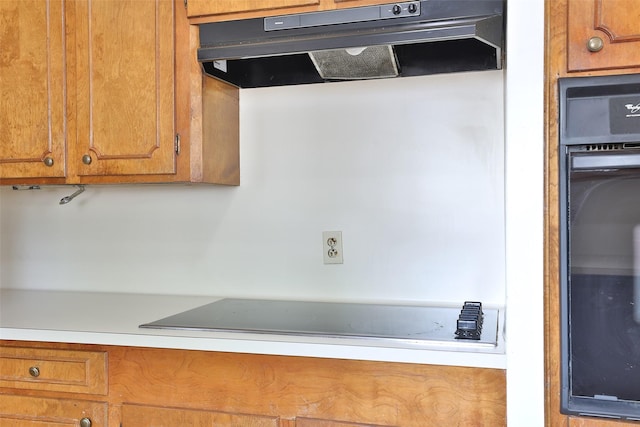 kitchen featuring brown cabinets, light countertops, under cabinet range hood, and black appliances
