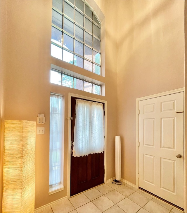 foyer featuring light tile patterned floors, a towering ceiling, and baseboards