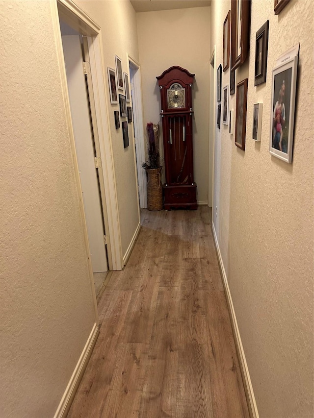 hallway featuring baseboards, wood finished floors, and a textured wall