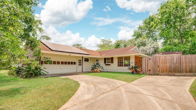 ranch-style home featuring roof mounted solar panels, fence, concrete driveway, a front yard, and a garage