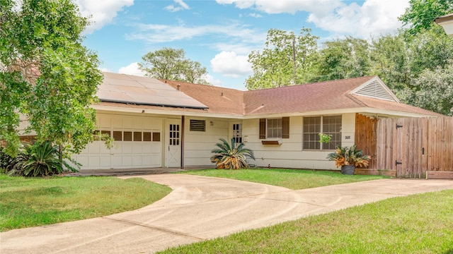 ranch-style house with a garage, concrete driveway, roof mounted solar panels, a front yard, and roof with shingles