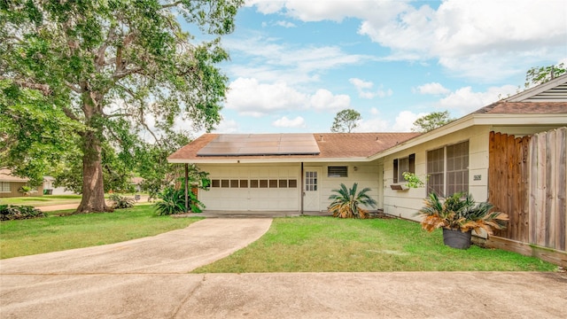 ranch-style house with roof mounted solar panels, driveway, fence, a front lawn, and a garage