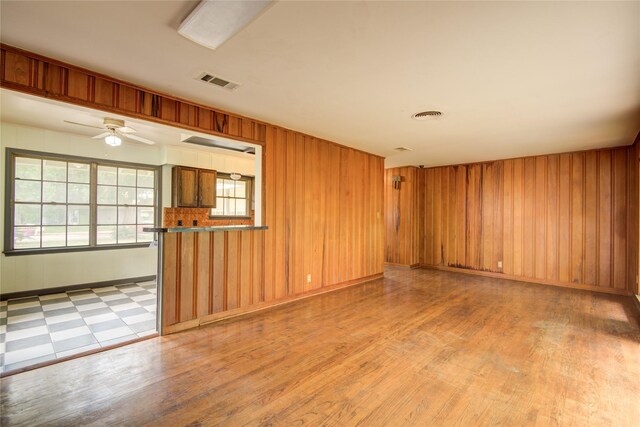 spare room with wood finished floors, visible vents, a ceiling fan, and wood walls