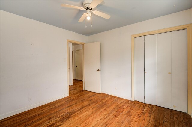 unfurnished bedroom featuring baseboards, wood finished floors, a closet, and ceiling fan