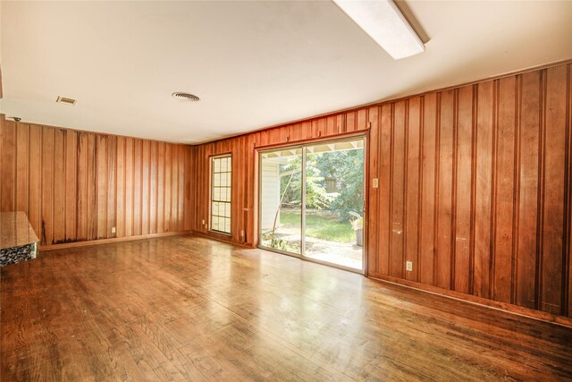 empty room with visible vents, wood walls, and wood finished floors