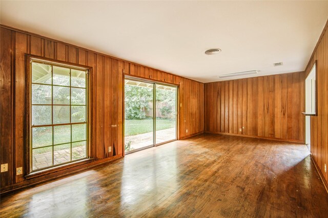 empty room featuring wood walls, wood finished floors, and a healthy amount of sunlight