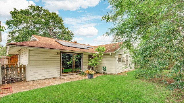 back of property with roof mounted solar panels, a shingled roof, fence, and a yard