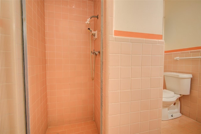 full bathroom featuring a tile shower, tile walls, toilet, and wainscoting