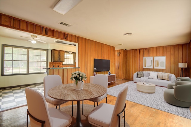 dining area featuring visible vents, ceiling fan, and wooden walls