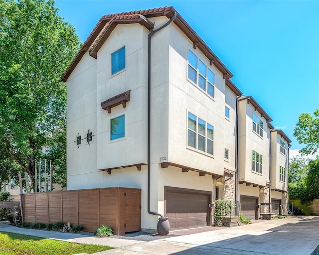 exterior space featuring fence, an attached garage, driveway, and stucco siding
