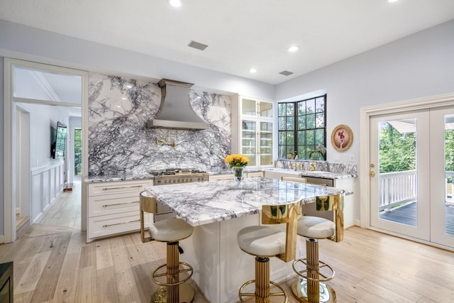 17003 Creeksouth Rd, Houston, TX 77068 - kitchen with custom range hood, light wood finished floors, light stone countertops, a breakfast bar area, and white cabinetry