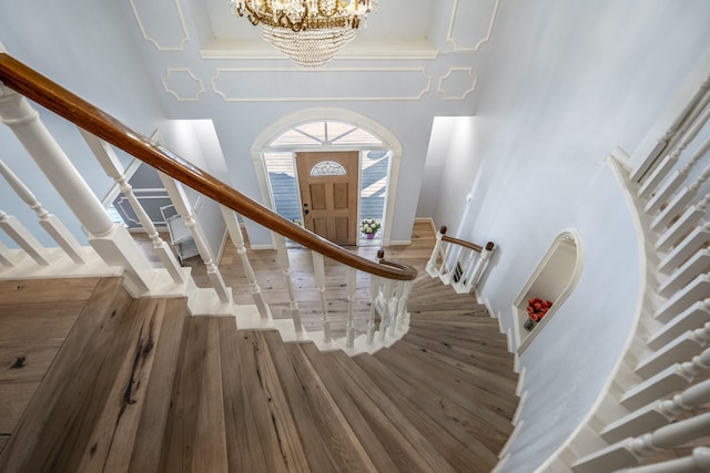 stairway with a towering ceiling, baseboards, wood finished floors, and a chandelier