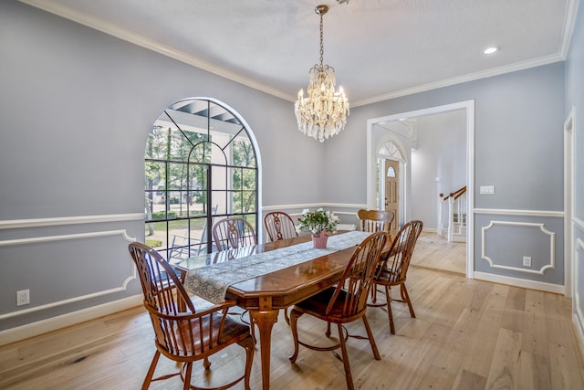 dining room with ornamental molding, a wainscoted wall, a chandelier, and light wood-type flooring
