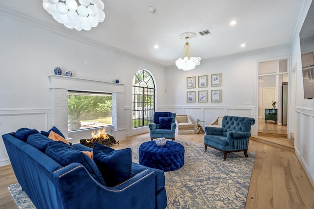 living room featuring light wood finished floors, visible vents, a chandelier, and crown molding