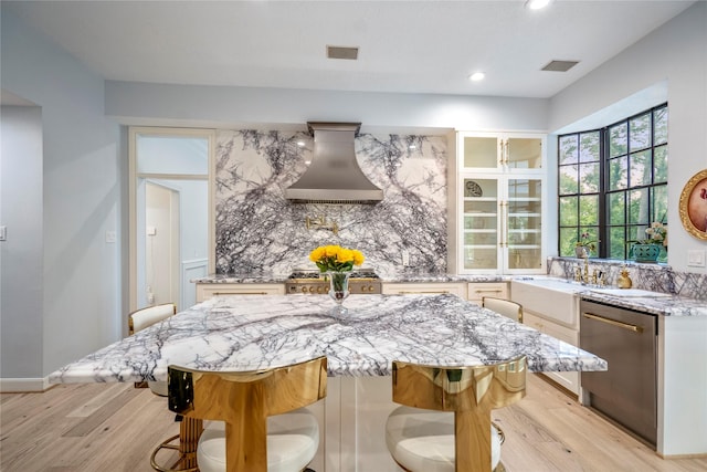 17003 Creeksouth Rd, Houston, TX 77068 - kitchen featuring dishwasher, wall chimney exhaust hood, light wood-type flooring, light stone countertops, and a kitchen breakfast bar