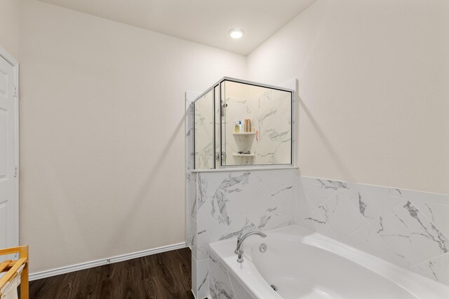full bath featuring a garden tub, a shower stall, wood finished floors, and baseboards