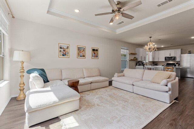 living area featuring a chandelier, wood finished floors, crown molding, ceiling fan, and a tray ceiling