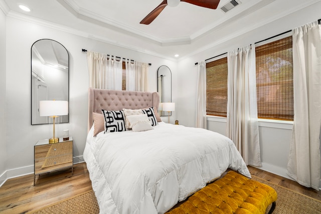 bedroom featuring recessed lighting, a tray ceiling, wood finished floors, visible vents, and ornamental molding