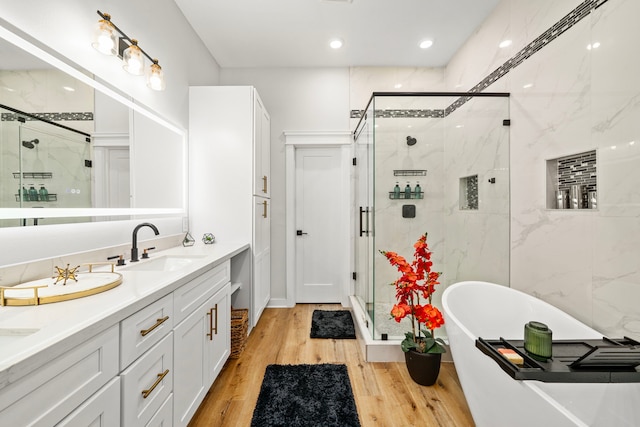 full bath featuring double vanity, wood finished floors, a sink, a soaking tub, and a stall shower