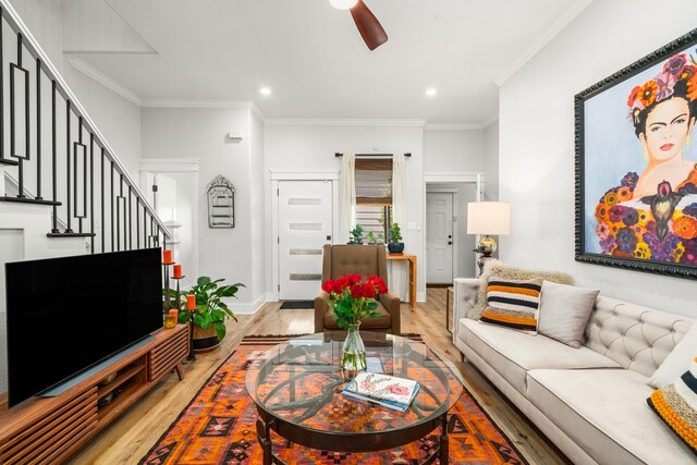 living room featuring light wood-style flooring, ornamental molding, stairway, and a ceiling fan