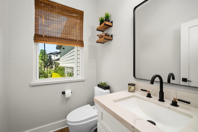 half bathroom featuring toilet, vanity, and baseboards