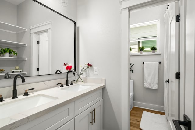 full bath with double vanity, wood finished floors, baseboards, and a sink