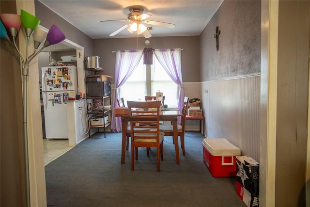 carpeted dining space featuring a ceiling fan and a wainscoted wall